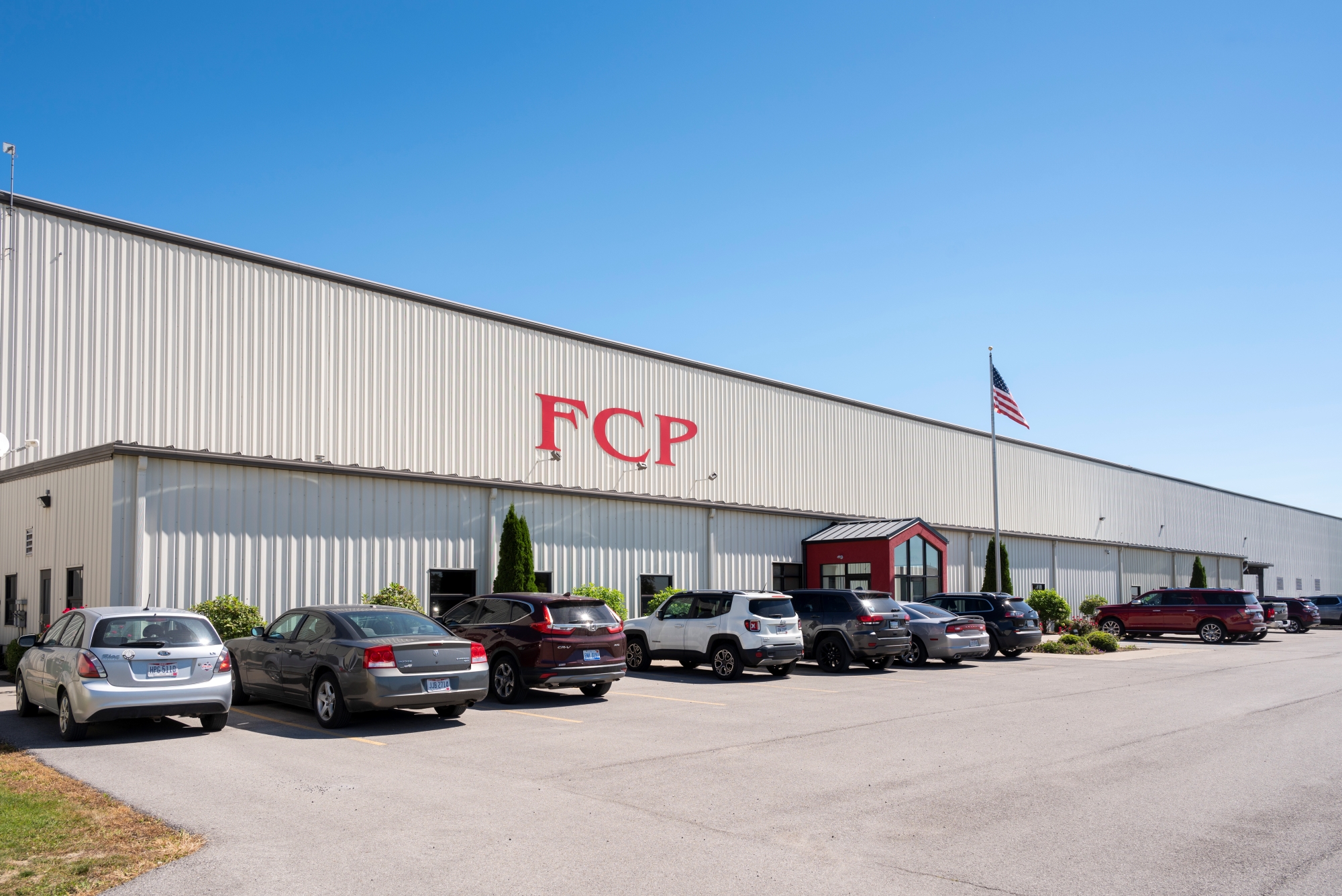 Fulton County Processing Facility Exterior White industrial building with FCP signage, parking lot, cars, and flag under a clear blue sky.